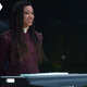 Captain Michael Burnham is sporting long braids and stands in maroon formal dress delivering a speech at a lectern.